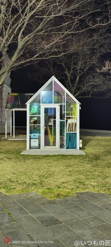 芝生のうえに立っているガラス張りの小屋を暗所撮影した写真 | モバイル比較レビュー.jp nubia Z70 Ultra カメラ 芝生のうえに立っているガラス張りの小屋を暗所撮影した写真